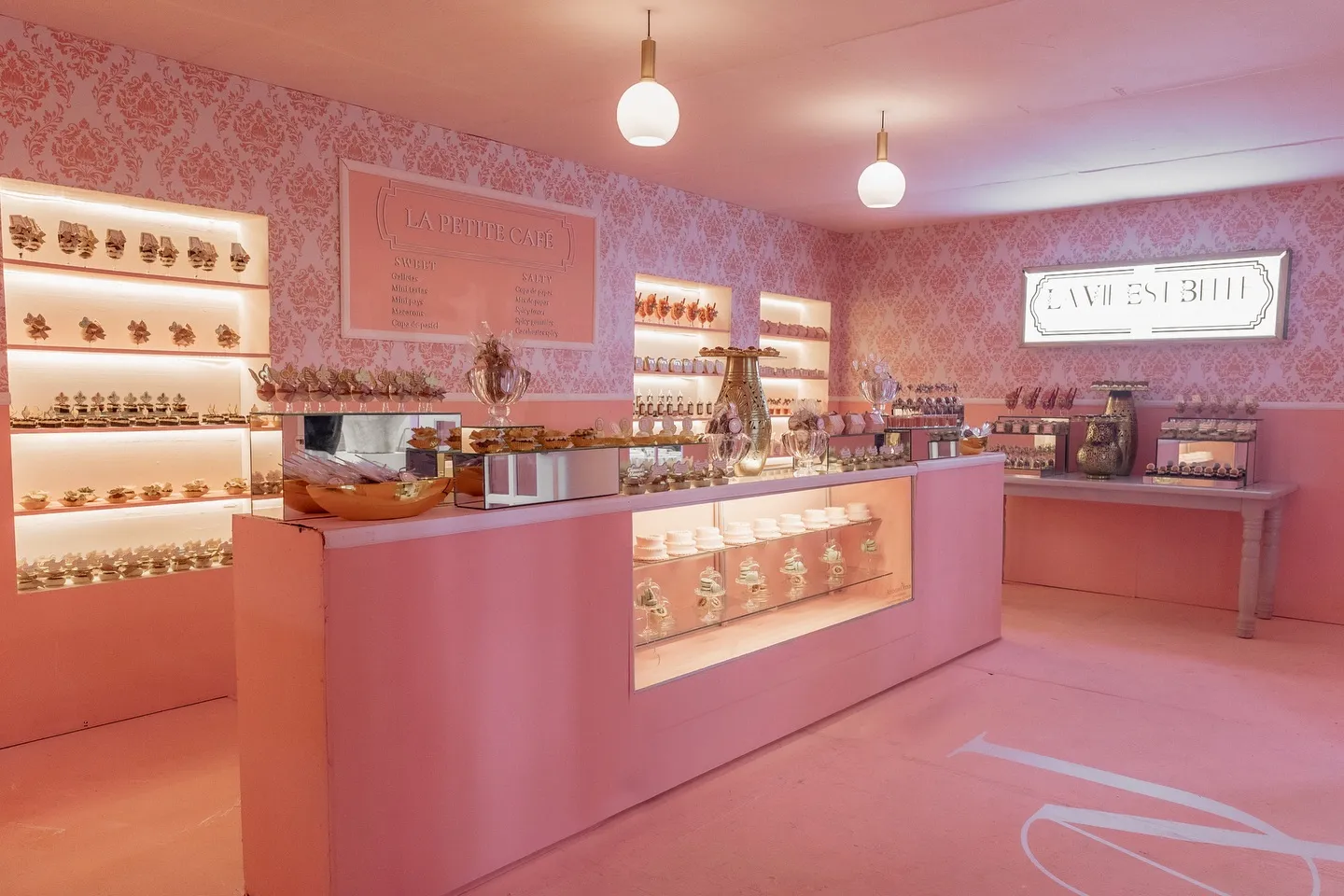 Barra de patisserie iluminada con vitrinas de postres sobre muro rosa