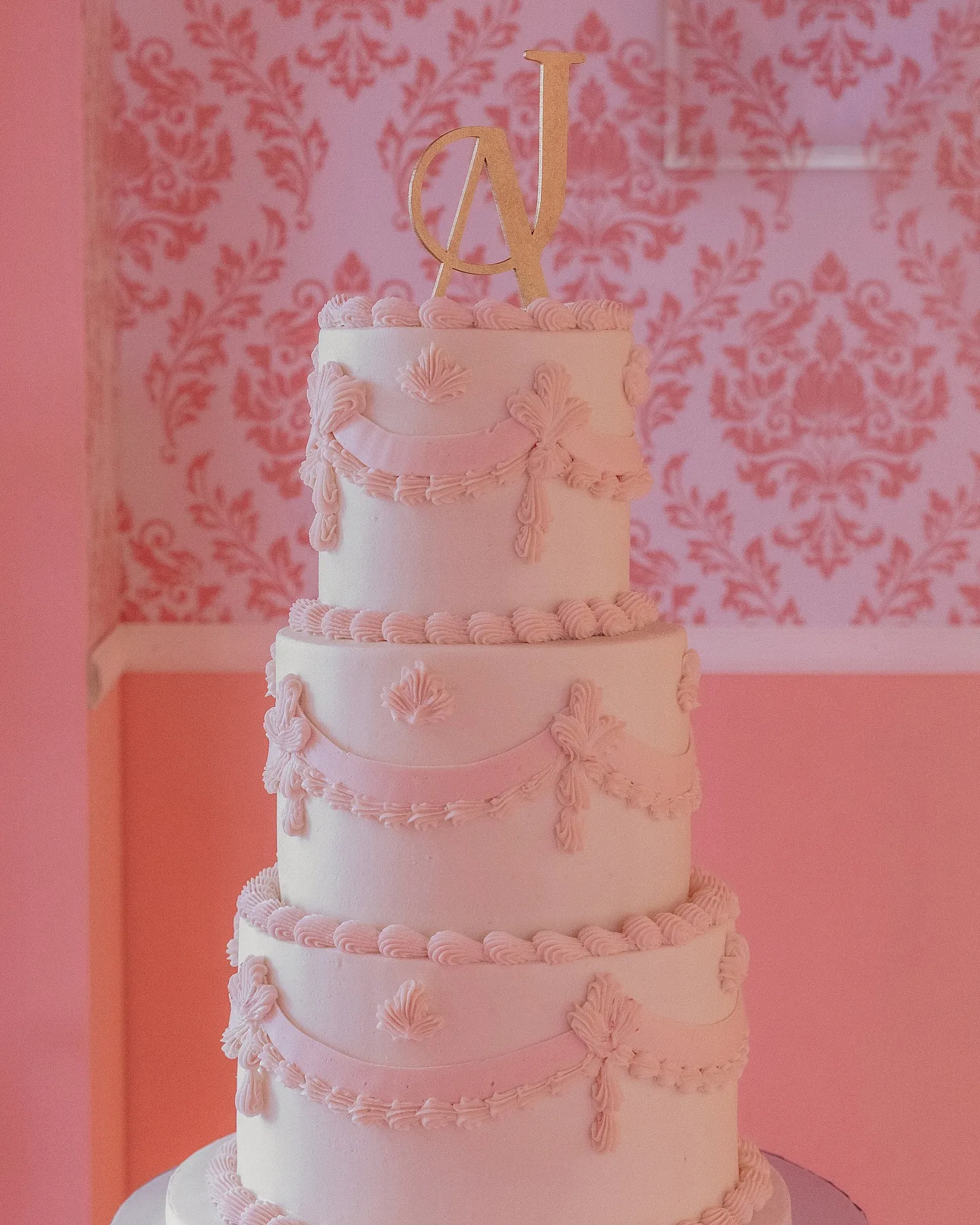 Pastel blanco de cuatro pisos frente a un muro de damasco rosa