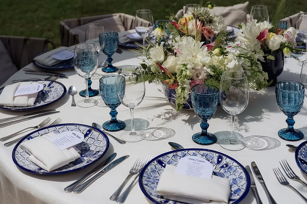 Mesa vestida con vajilla de talavera, cristalería azul y flor de temporada
