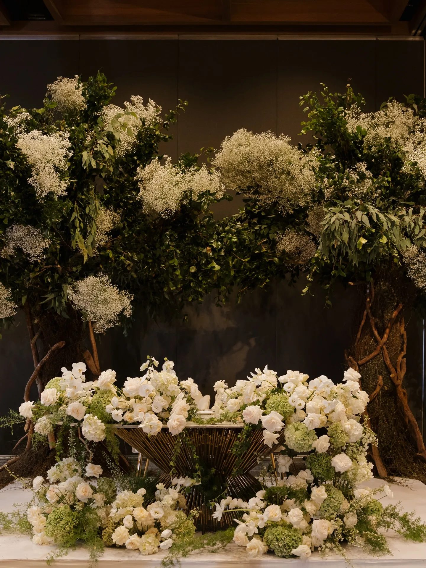 Instalación floral blanca montada a nivel de piso frente al muro del salón
